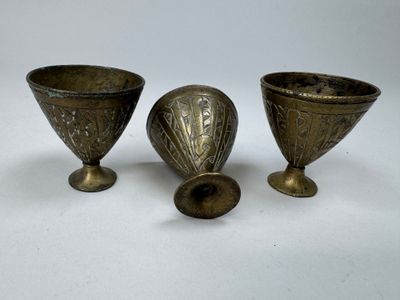 Trois vases en laiton ancien sont posés sur une surface blanche