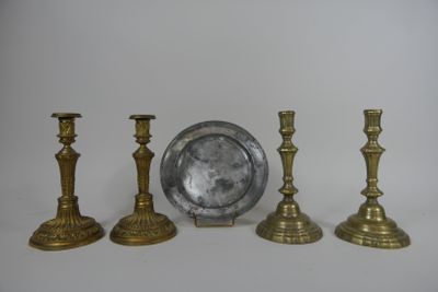 three brass candlesticks and a silver plate on a white surface
