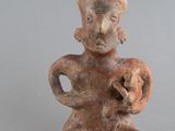 une vieille figurine représentant un homme tenant une poire, à côté d'une petite figurine représentant un homme