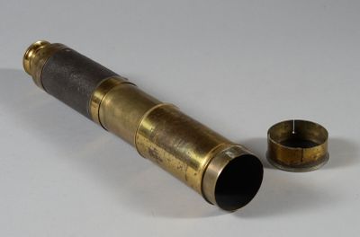 a brass telescope on a white surface next to a cup