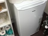 un petit réfrigérateur dans un coin de la pièce, sur lequel sont posés des rouleaux de papier toilette