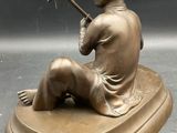 statue of a boy sitting on a rock with a stick
