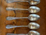 six silver spoons are lined up on a wooden table