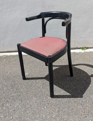 une chaise noire avec une assise rose, posée sur le trottoir