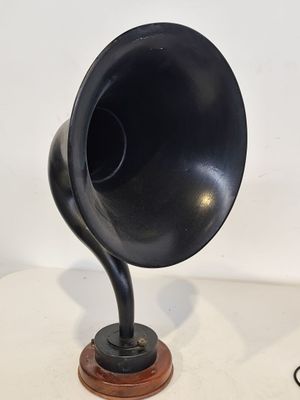 un gramophone noir posé sur un socle en bois, sur une table blanche