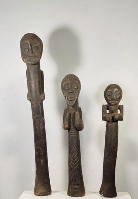 trois statues en bois représentant des personnages, posées sur un socle blanc