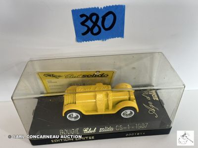un camion jaune dans une vitrine, sur lequel est accrochée une pancarte