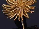 un gros plan d'une broche en forme de fleur dorée posée sur une surface noire