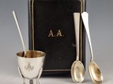 two silver spoons and a silver cup with a book in the background