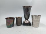 quatre tasses en métal de formes différentes et un vase en argent posés sur une surface blanche