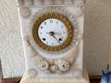 une horloge blanche posée sur une table, à côté d'un vase bleu