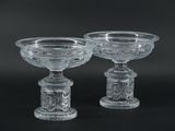 pair of clear glass footed bowls on pedestals against a black background
