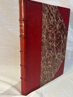 an old book with a red cover sitting on a white surface