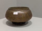 un vase marron posé sur une table, sur lequel est collé un autocollant