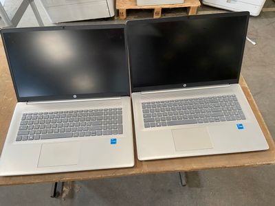 Deux ordinateurs portables sont posés sur une table, devant une pile de cartons.