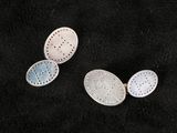 two silver spoons with holes on them sitting on a black surface