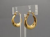 un gros plan sur une paire de boucles d'oreilles créoles en or posées sur un présentoir transparent