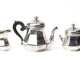 three silver teapots and two silver cups on a white surface