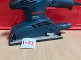 une ponceuse orbitale Bosch posée sur une table, à côté d'une boîte rouge