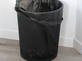 a black trash can sitting on the floor next to a white wall
