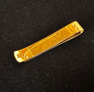 gold plated tie bar on black cloth with a gold design