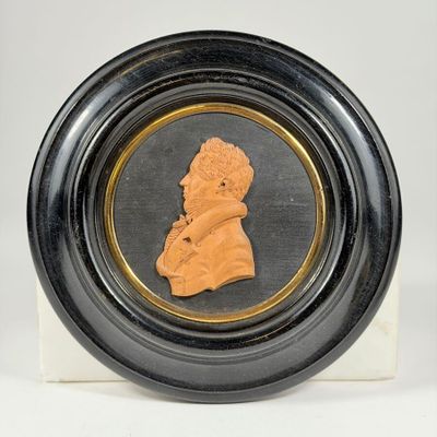 a close up of a black and gold plate with a bust of a man