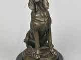 statue en bronze représentant un chien assis sur un socle, sur fond blanc