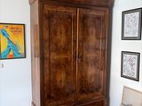 une grande armoire en bois dans une pièce où sont accrochés des tableaux au mur
