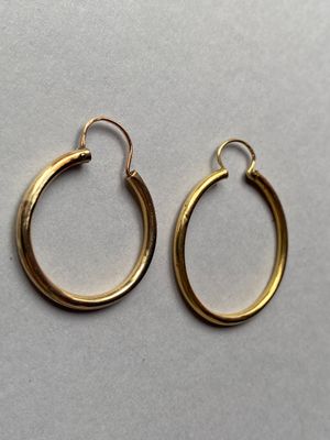 deux paires de boucles d'oreilles créoles en or posées sur une surface blanche