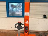 un chariot élévateur orange dans un entrepôt, avec une télévision en arrière-plan