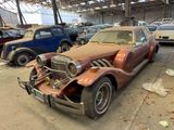 a rusted old car in a garage with other cars in the background