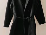black coat on a hanger on a white wall with a black shirt underneath it