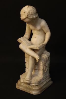 a statue of a boy sitting on a rock reading a book