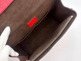 a person holding a brown purse with a red handle