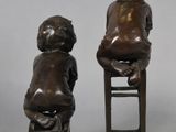 pair of bronze figurines of children sitting on stools