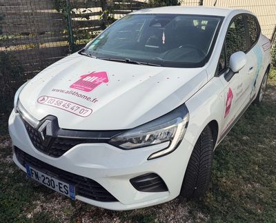 La voiture blanche est garée sur l'herbe, devant une clôture.