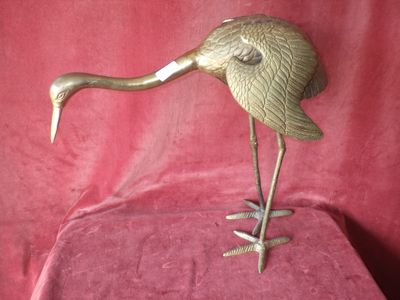 figurine de grue en laiton sur socle, sur fond de velours rouge