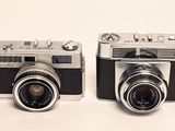 two cameras sitting next to each other on a white surface