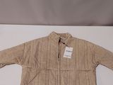 La veste pour enfant est de couleur beige et comporte une étiquette blanche.
