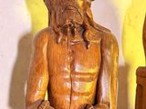 une statue en bois représentant un homme assis sur une table, à côté d'un vase
