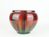 a red and green vase sitting on a white surface