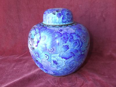 un vase bleu muni d'un couvercle, posé sur un tissu rouge