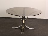 une table en verre avec un piètement en métal, posée sur un sol recouvert de moquette