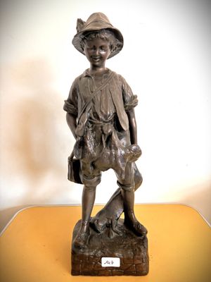 une statue en bronze représentant un garçon avec un chien, posée sur une table