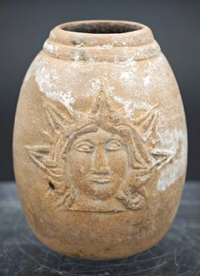 un pot en terre cuite orné d'un visage, posé sur une table