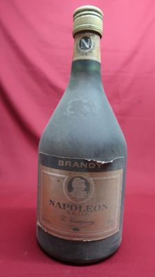 an old bottle of brandy sitting on a red cloth