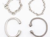 three pairs of silver bracelets and a ring on a white surface
