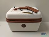 une valise blanche avec une poignée marron et une étiquette dessus
