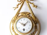 an image of a gold clock hanging on a wall on a white background