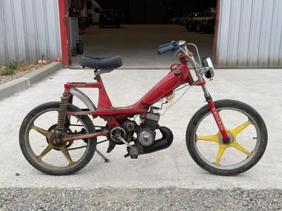 une petite moto rouge garée devant un garage